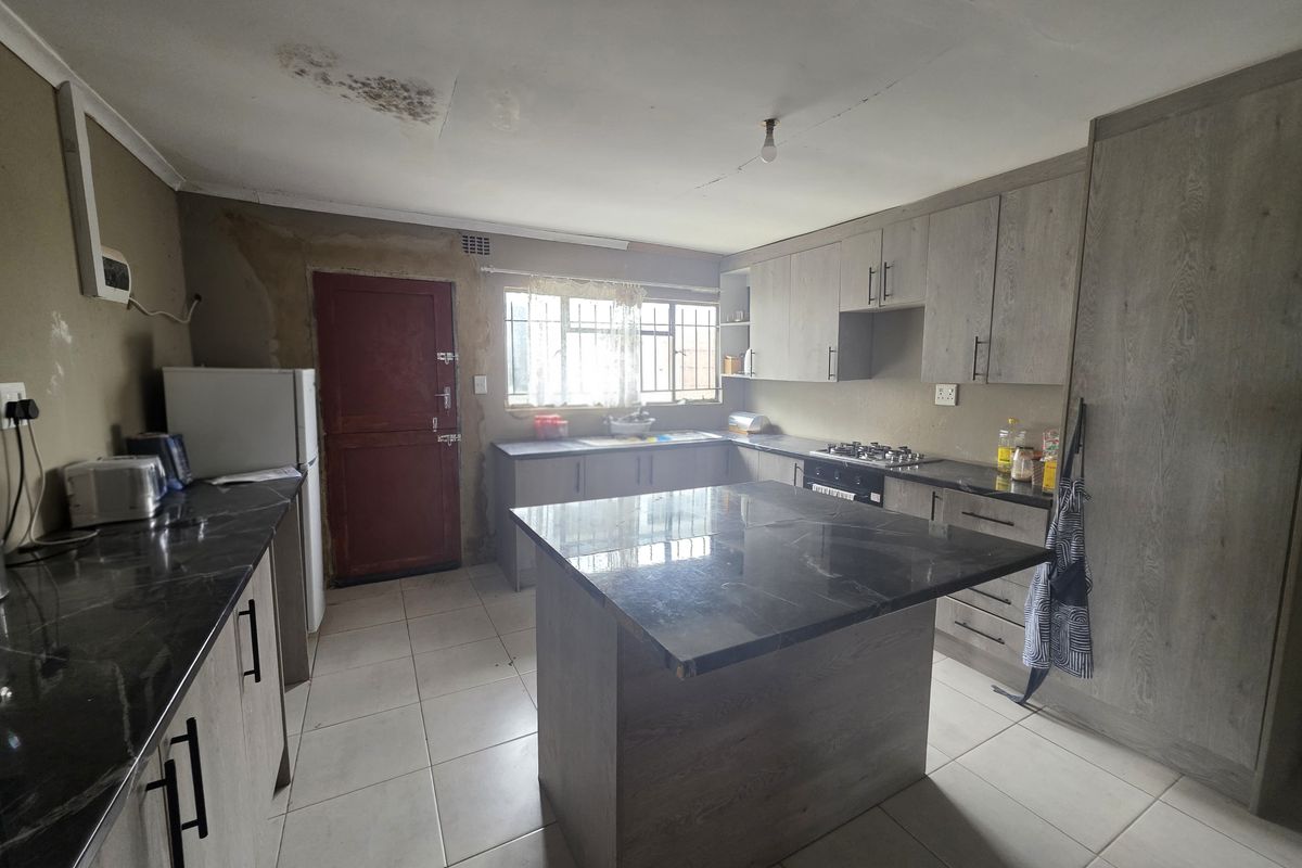 A kitchen featuring grey cabinetry, a central island with a dark countertop, tiled flooring, and a built-in gas hob.