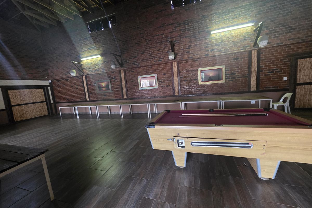 Spacious lodge entertainment area featuring exposed brick walls, tiled flooring, and high vaulted ceilings, currently set up with a pool table.