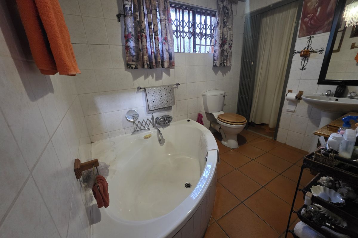 A functional bathroom featuring a corner bathtub, pedestal sink, and toilet, finished with tiled walls and flooring.