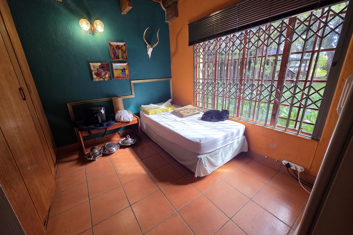 A bedroom featuring terracotta floor tiles, built-in wooden cabinetry, and security bars on the window, offering a rustic aesthetic.