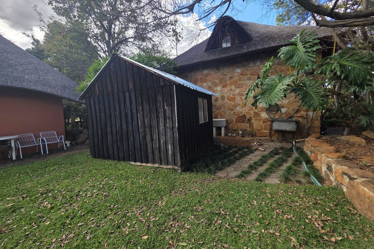 A rustic farm exterior featuring a stone-walled building with a thatched roof, a wooden storage shed, and a paved utility area with a sink.