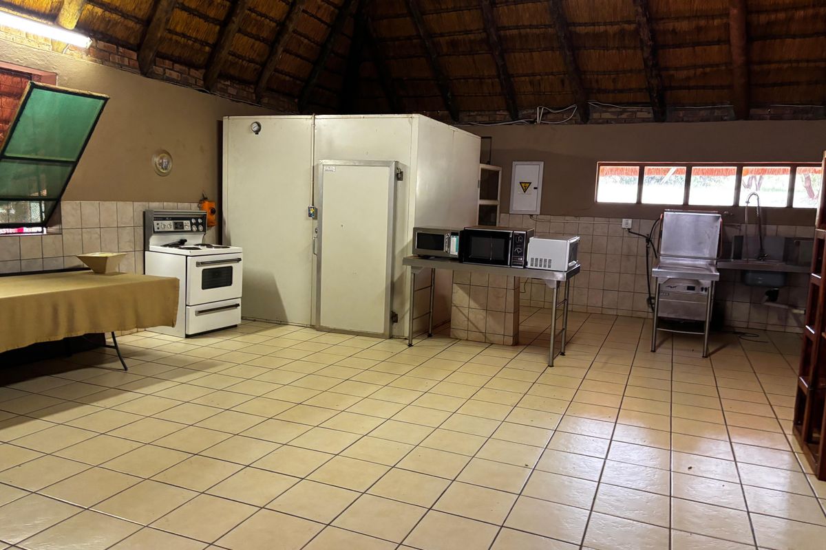 Commercial-style kitchen area featuring a large walk-in cold room, tiled flooring, and a high thatched roof with exposed timber beams.