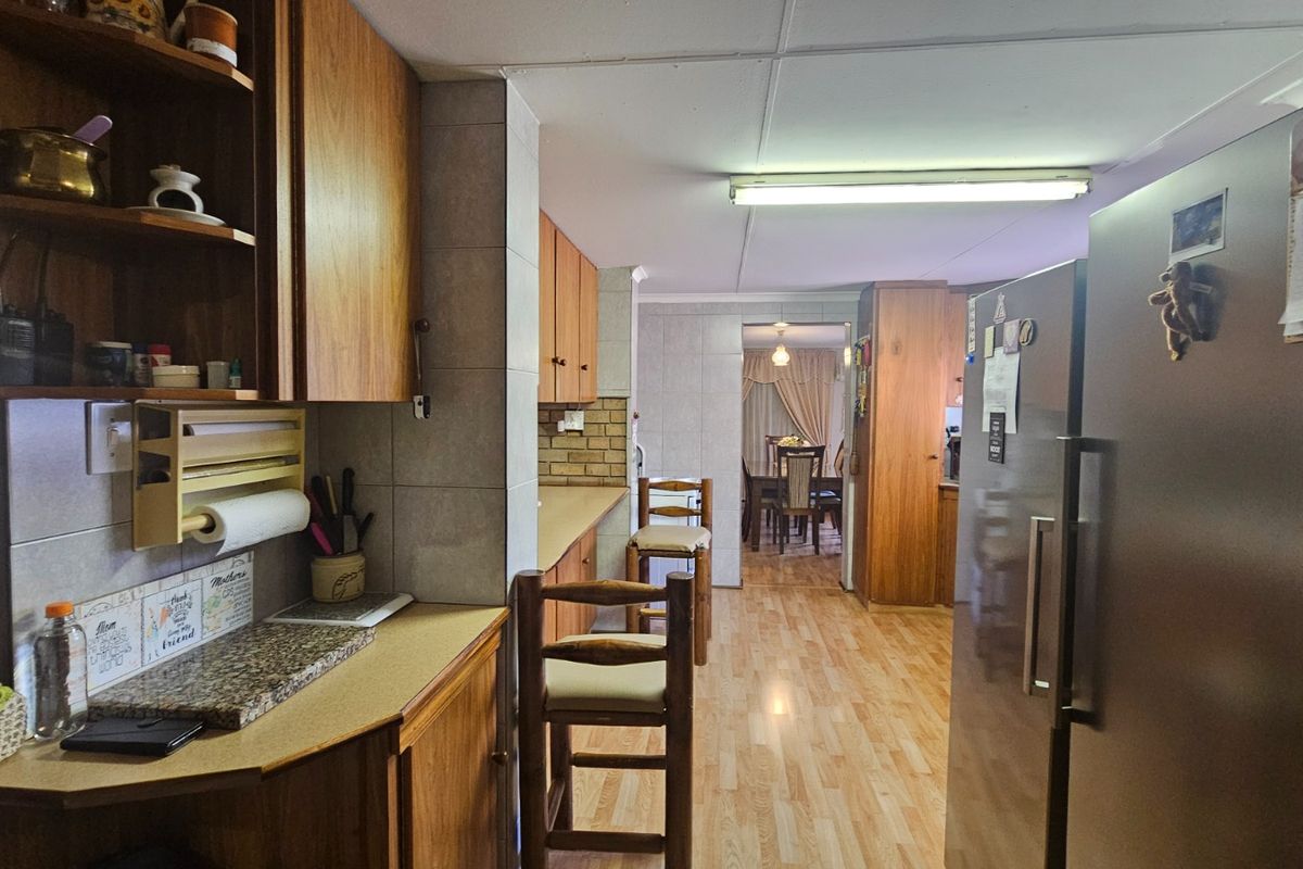A functional kitchen featuring wood-finish cabinetry, tiled splashbacks, and laminate flooring, with an open-plan layout leading into the dining area.