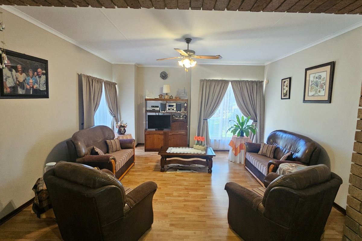 A spacious living room featuring laminate wood flooring, a ceiling fan, and exposed brick accents, providing a comfortable and functional family living space.