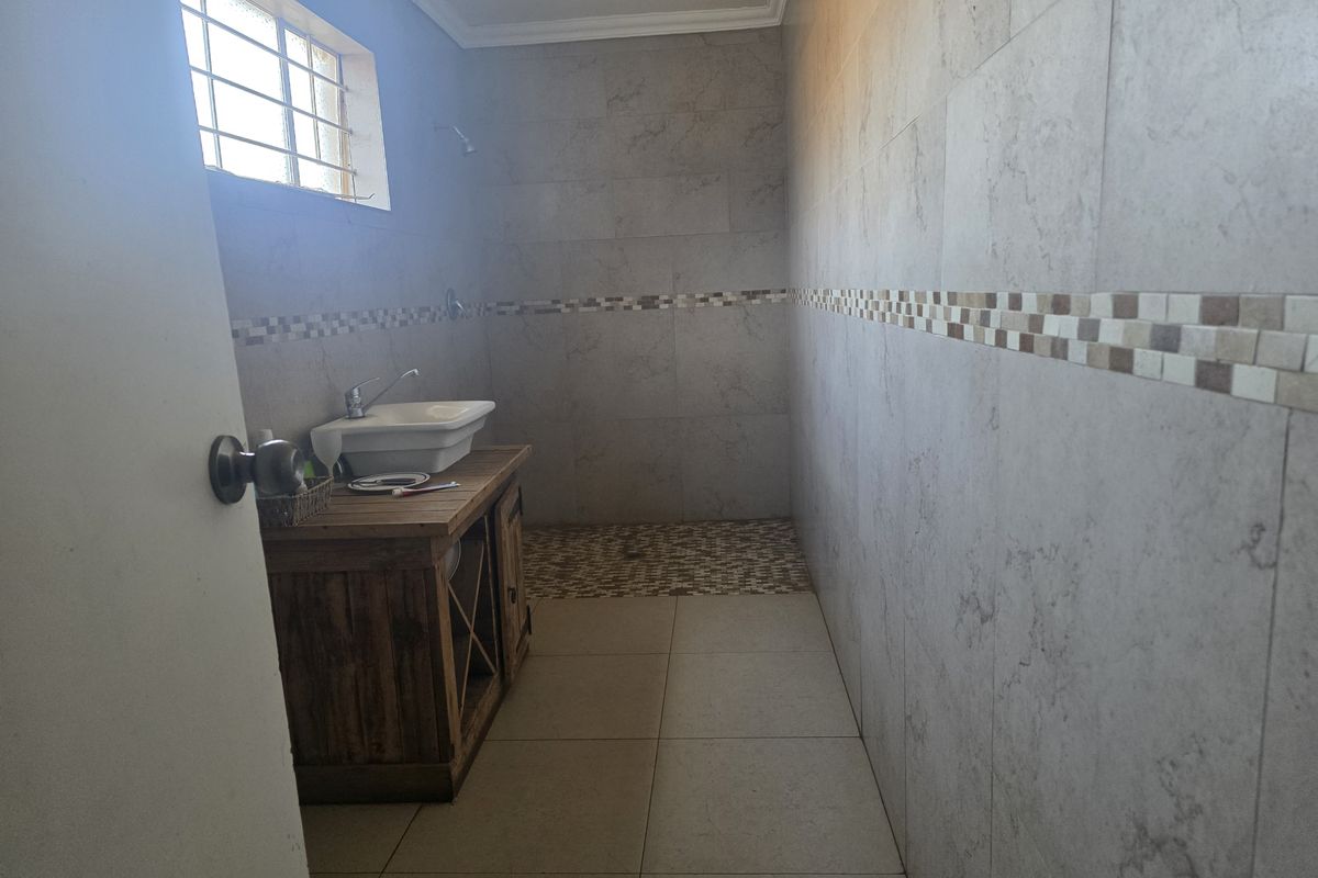 A functional bathroom featuring a vessel sink on a wooden vanity, neutral wall tiling with a decorative mosaic border, and a walk-in shower area.