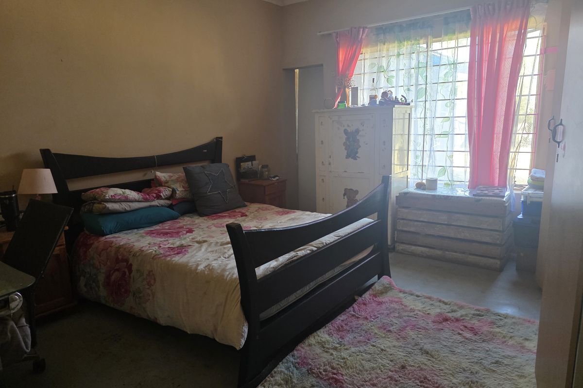 A standard bedroom featuring a window with security bars and neutral wall finishes, offering a functional space for rest.