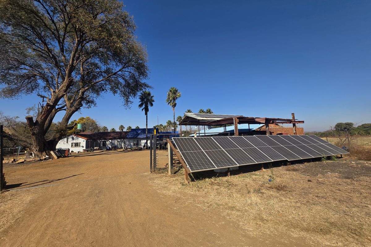 Exterior view of the farm property featuring a ground-mounted solar panel array, outbuildings, and a large mature tree on the grounds.