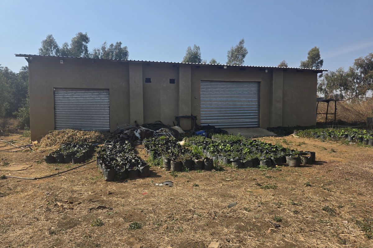 Exterior view of a farm utility building featuring two roller shutter doors and a corrugated metal roof, set on an unpaved rural plot.