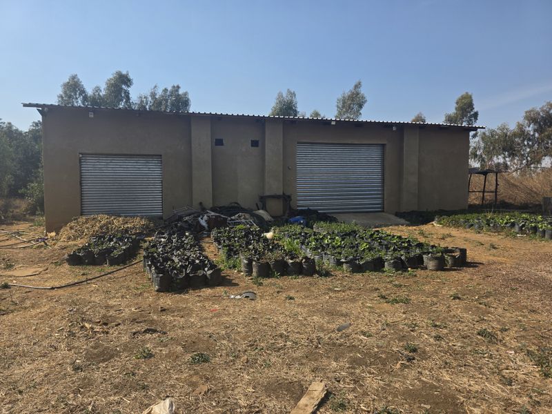 Exterior view of a farm utility building featuring two roller shutter doors and a corrugated metal roof, set on an unpaved rural plot.