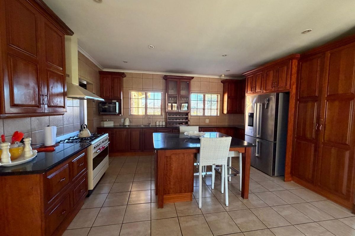 Spacious kitchen featuring warm-toned wooden cabinetry, a central island with a dark stone countertop, tiled flooring, and integrated stainless steel appliances.