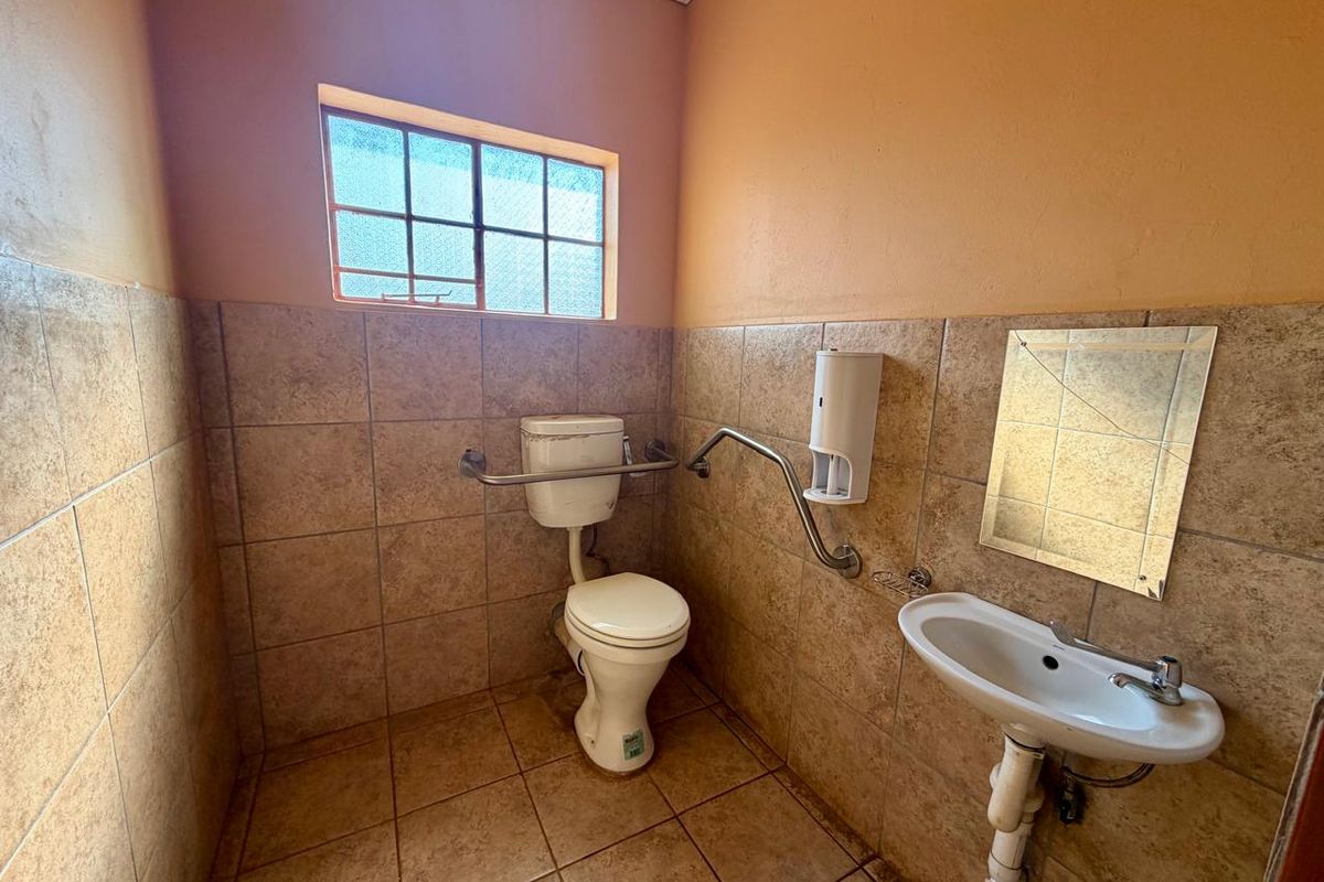 A functional office bathroom featuring tiled walls and flooring, equipped with a toilet, washbasin, and accessibility grab rails.