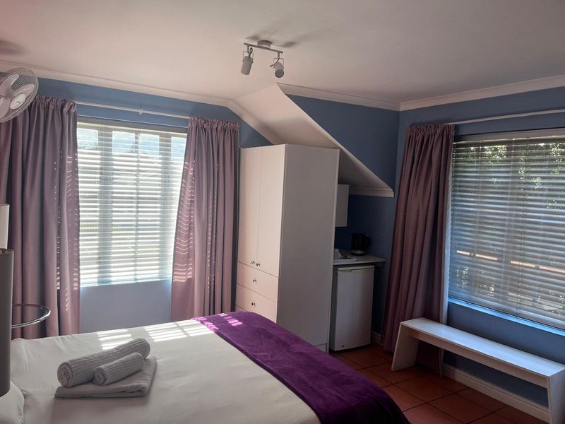 A bedroom featuring tiled flooring, a built-in wardrobe, and a sloped ceiling, with dual windows providing natural light.