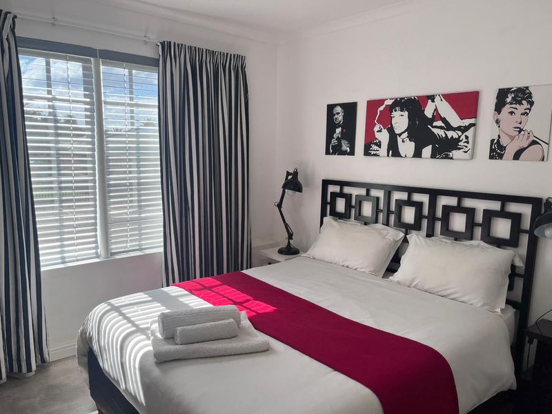 A well-maintained bedroom featuring neutral walls, window blinds, and curtain tracks, providing a clean and functional space for guests.