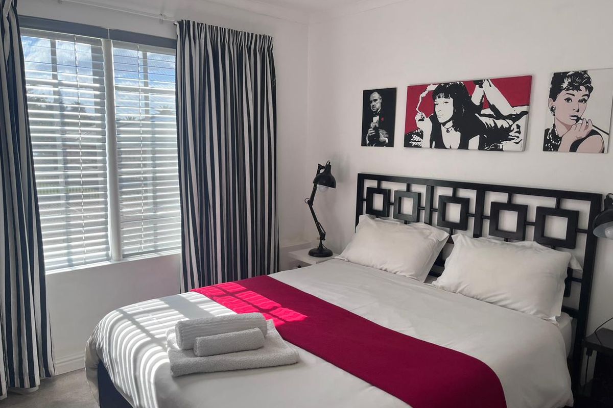 A well-maintained bedroom featuring neutral walls, window blinds, and curtain tracks, providing a clean and functional space for guests.
