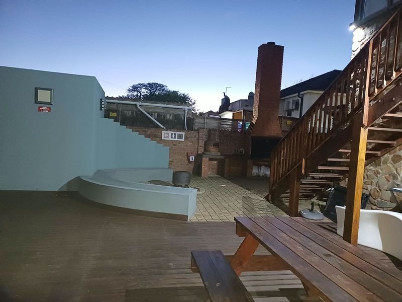 Outdoor entertainment area featuring a built-in brick braai, chimney, wooden staircase, and a combination of paved and decked flooring.