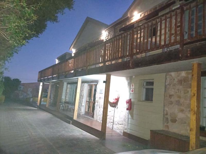 Front exterior view of a guest house featuring stone cladding, a wooden balcony, and paved driveway access at dusk.