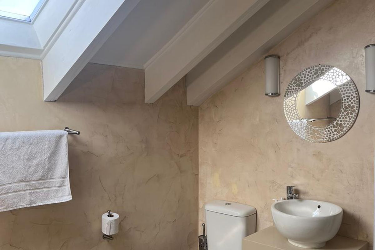 A modern bathroom featuring a skylight, exposed ceiling beams, a wall-mounted basin, and a toilet with textured wall finishes.