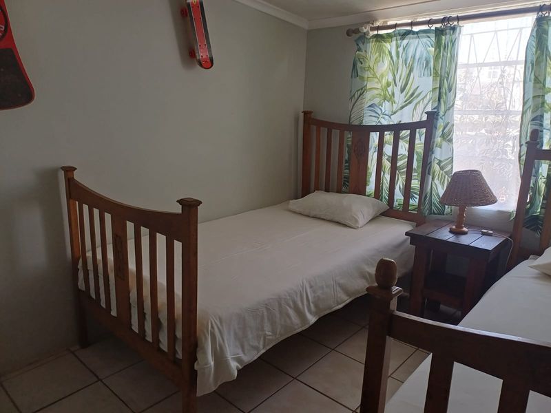 A functional bedroom featuring tiled flooring and a window fitted with security bars, providing a simple and practical sleeping space.