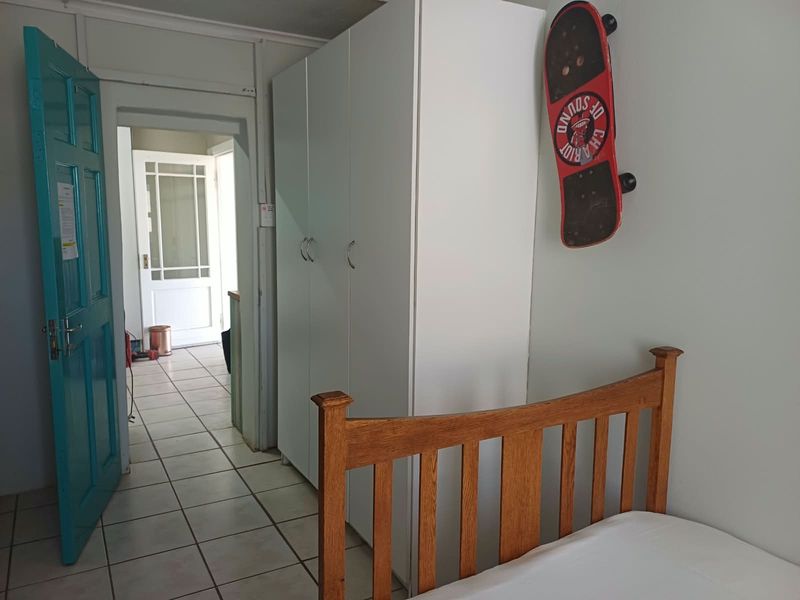 A bedroom featuring tiled flooring, a built-in wardrobe, and a view through to an adjacent hallway with a glass-paneled door.