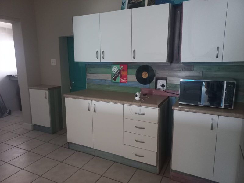A functional kitchen area featuring white laminate cabinetry, tiled flooring, and a built-in microwave, with a rustic wood-paneled backsplash.