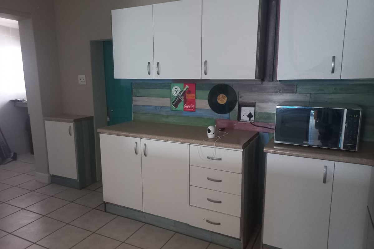 A functional kitchen area featuring white laminate cabinetry, tiled flooring, and a built-in microwave, with a rustic wood-paneled backsplash.