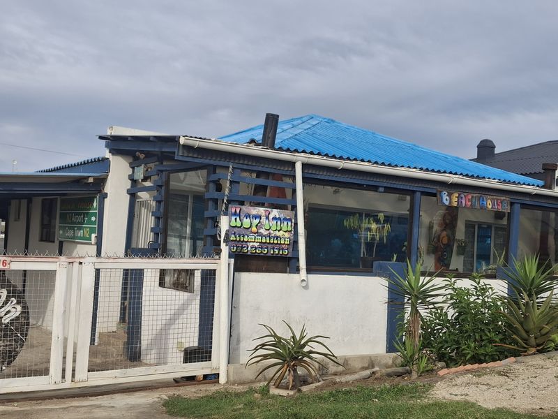 Front exterior view of the guest house featuring a gated entrance, blue corrugated metal roof, and timber pergola structure.