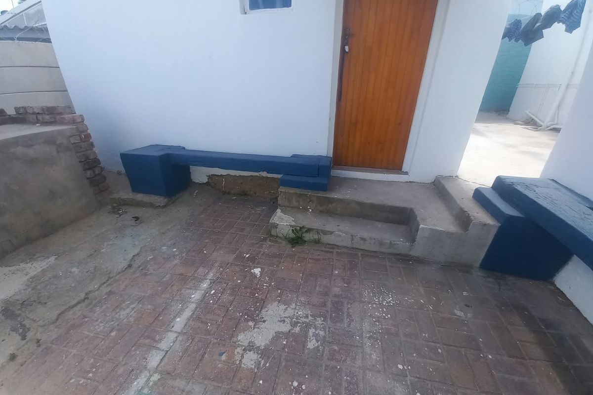Rear exterior patio area featuring built-in concrete seating, paved flooring, and access to the building via a wooden door.