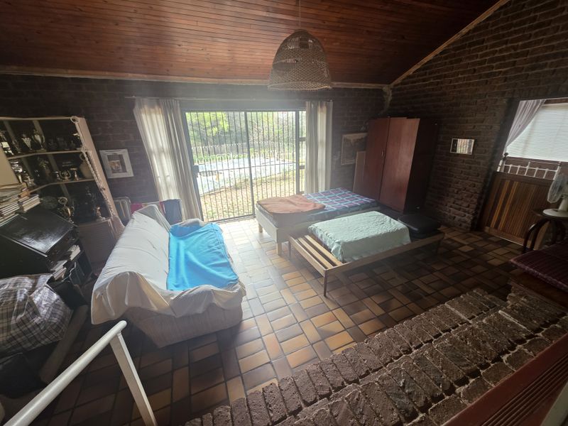 Spacious bedroom featuring exposed brick walls, a high timber raked ceiling, and terracotta tile flooring, with direct access to the outdoor area.
