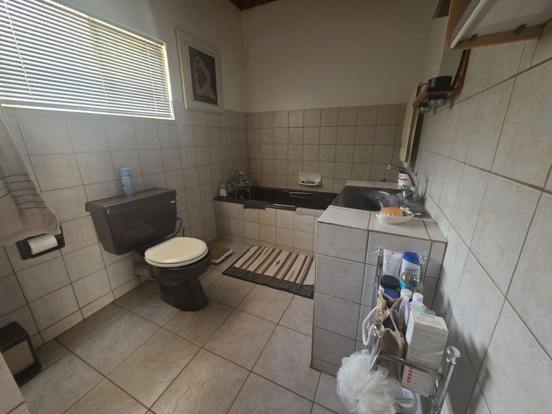 A dated bathroom featuring a built-in bathtub, tiled vanity with basin, and wall-mounted toilet, finished with neutral wall and floor tiles.