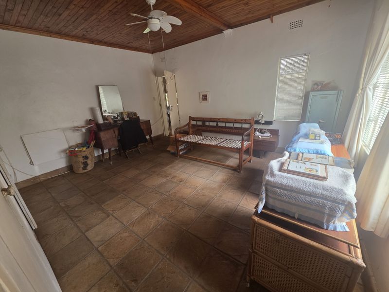 A bedroom featuring a timber-clad ceiling, ceiling fan, and tiled flooring, offering a functional space with potential for cosmetic updates.