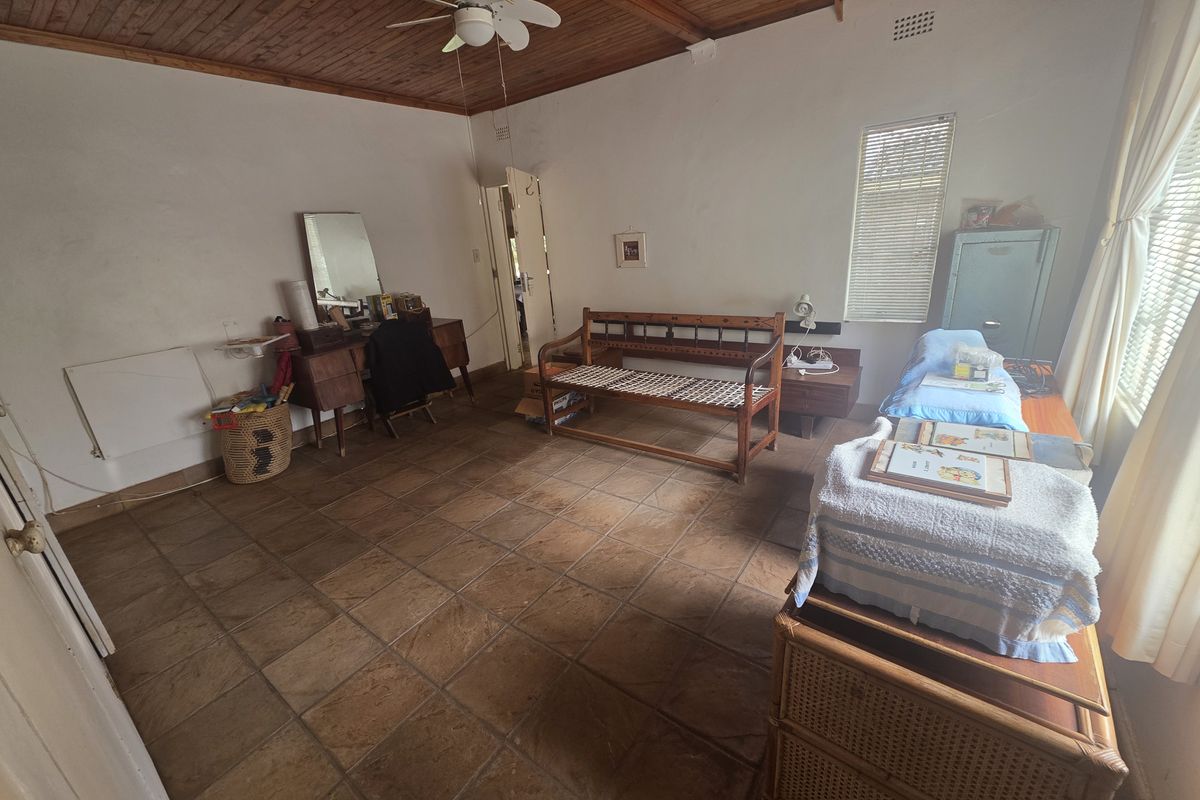A bedroom featuring a timber-clad ceiling, ceiling fan, and tiled flooring, offering a functional space with potential for cosmetic updates.