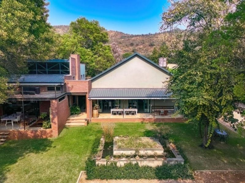 Aerial view of the rear elevation featuring a spacious covered patio, brick architecture, and a landscaped garden with a central water feature.