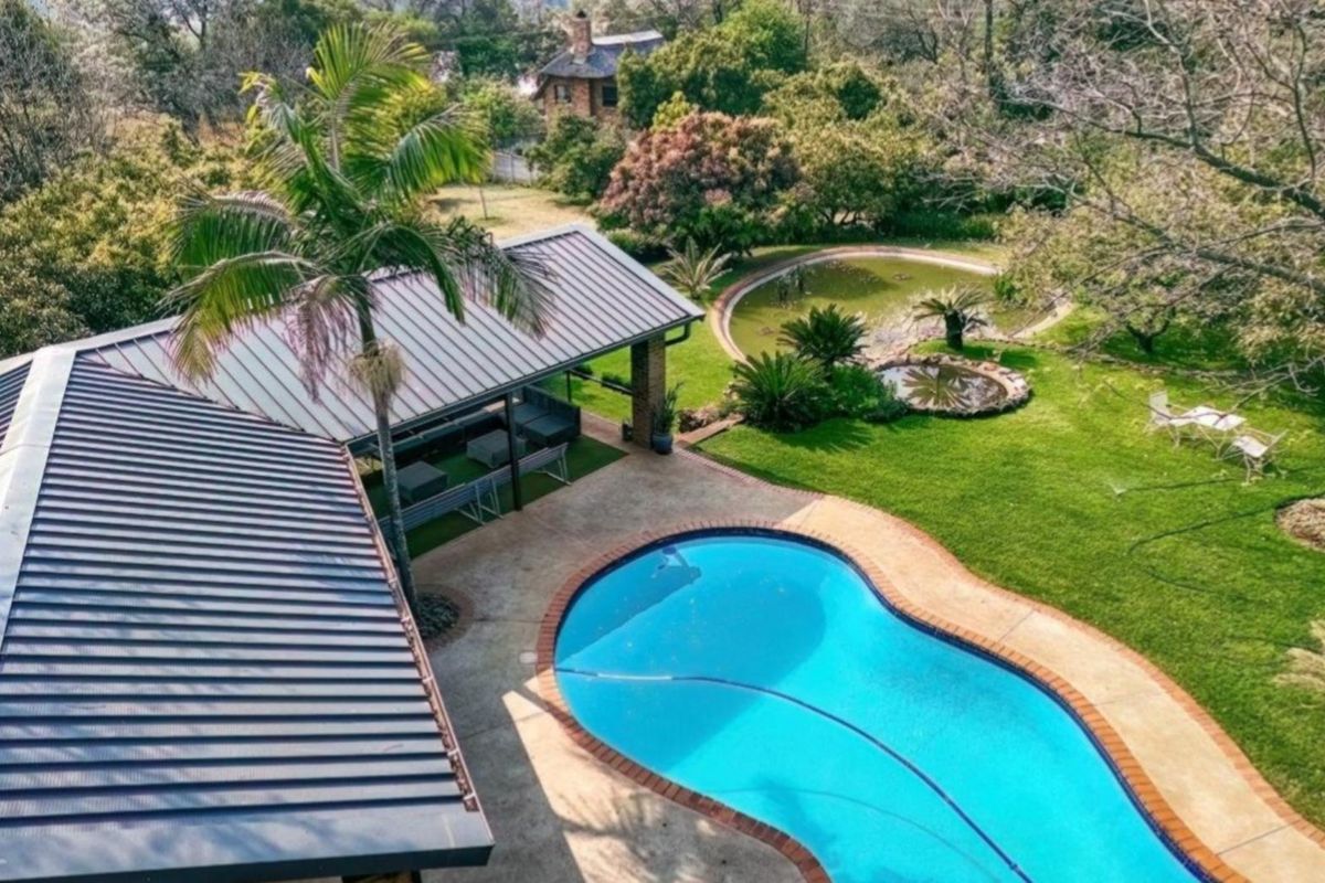 Aerial view of a small holding featuring a swimming pool, covered patio area, and a well-maintained garden with an ornamental pond.