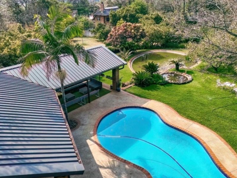 Aerial view of a small holding featuring a swimming pool, covered patio area, and a well-maintained garden with an ornamental pond.