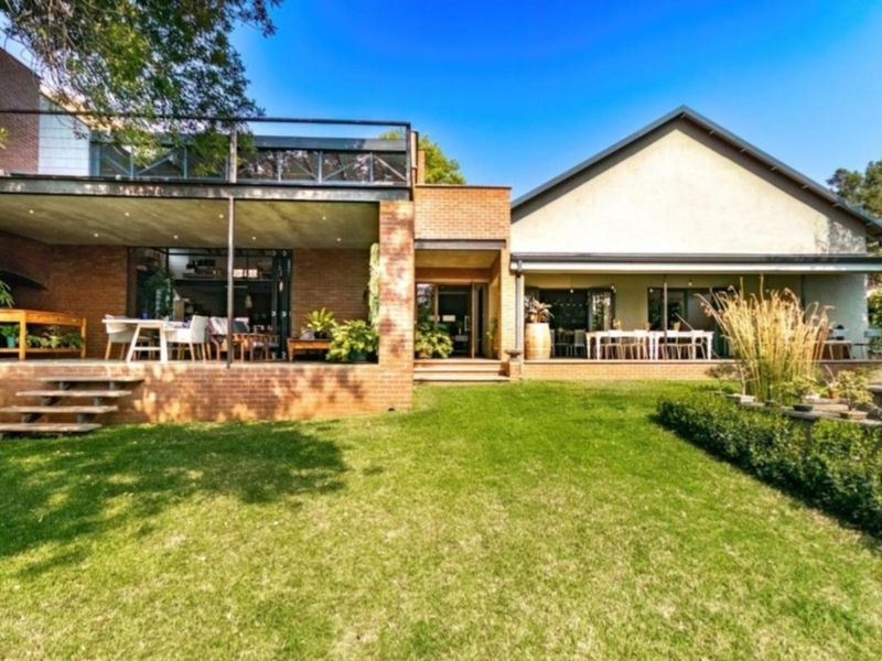 Spacious rear exterior view of the property featuring a large lawn, covered patio area, and an upper-level balcony with brick and plaster finishes.