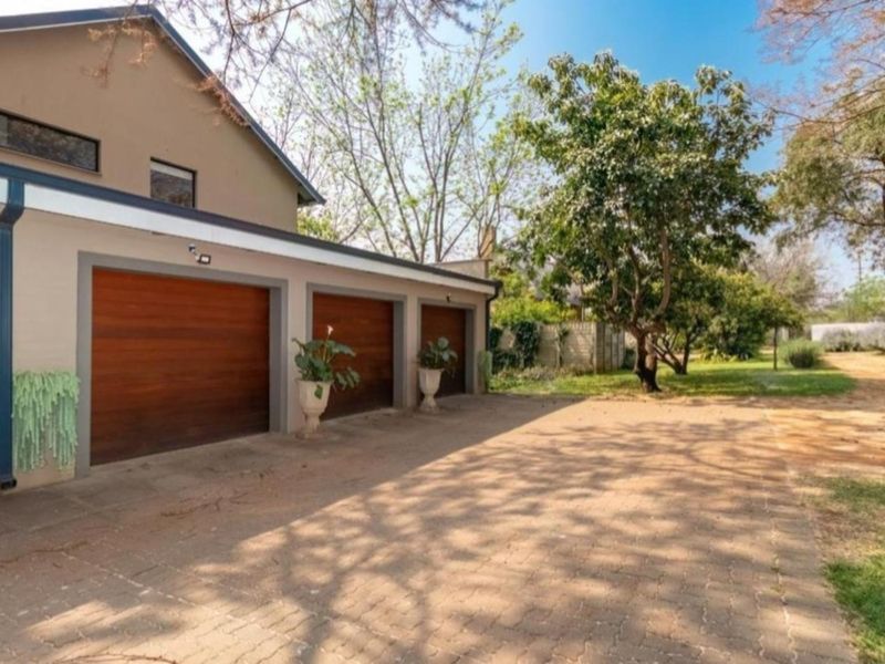 A triple garage with wooden doors and a paved driveway, situated on a small holding with mature trees and landscaped surroundings.