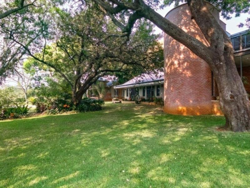 A view of the rear garden featuring a unique cylindrical brick structure, mature trees, and a covered patio area.