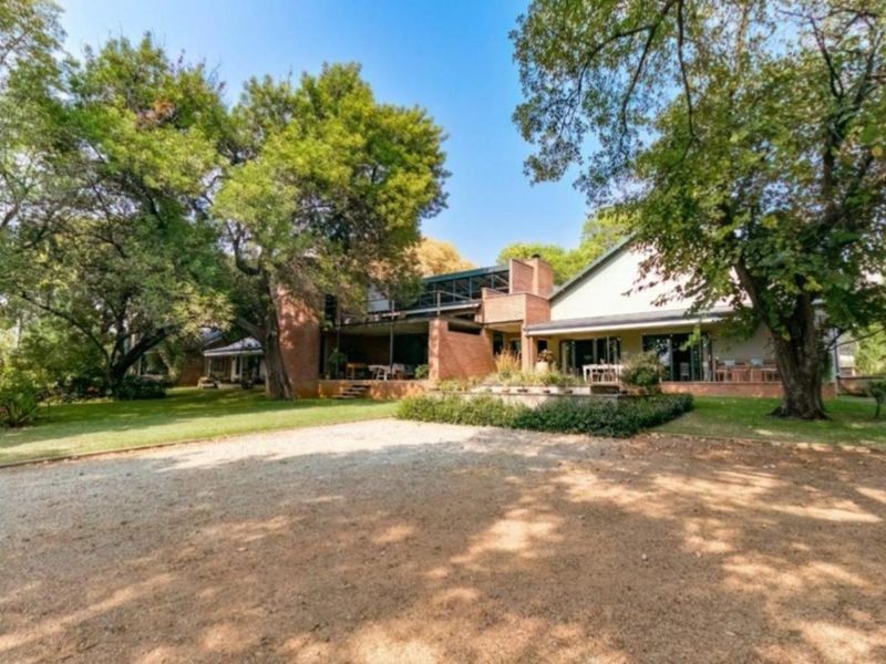 A spacious rear exterior view of the property featuring a brick facade, covered patio, balcony, and mature landscaped garden.