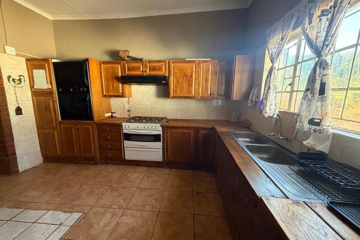 A functional kitchen featuring wooden cabinetry, a gas stove with extractor fan, double basin sink, and tiled flooring with a tiled backsplash.