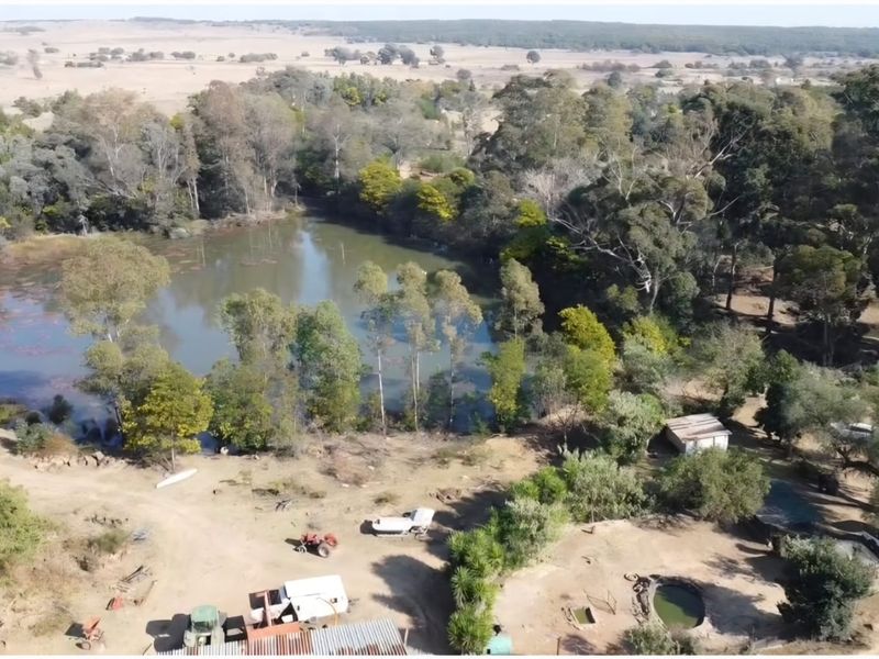 Aerial view of the farm property featuring a large natural dam surrounded by mature trees and open landscape.