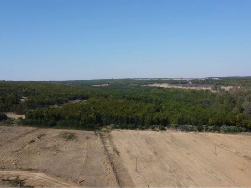 An aerial view of the expansive farm property, showcasing open fields, grazing land, and surrounding natural woodland.