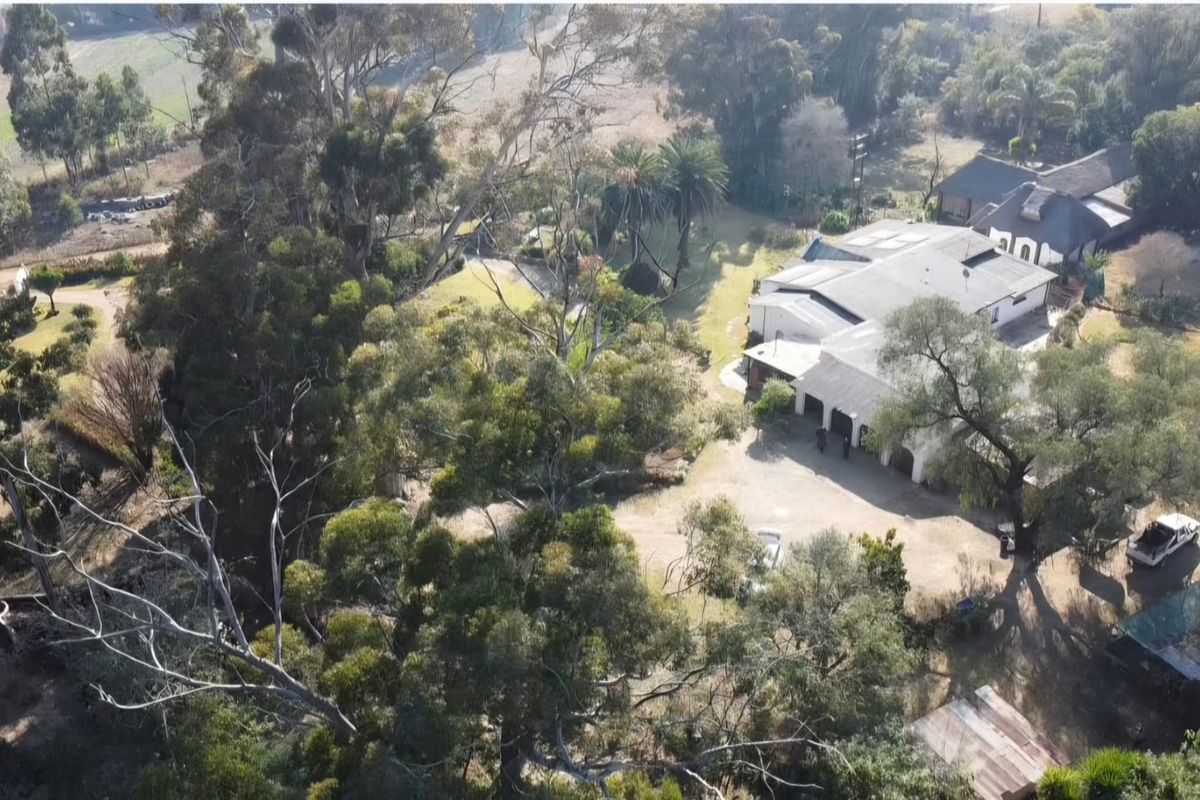 Aerial view of a farm property featuring a large residence with a thatched roof, expansive grounds, and mature trees.