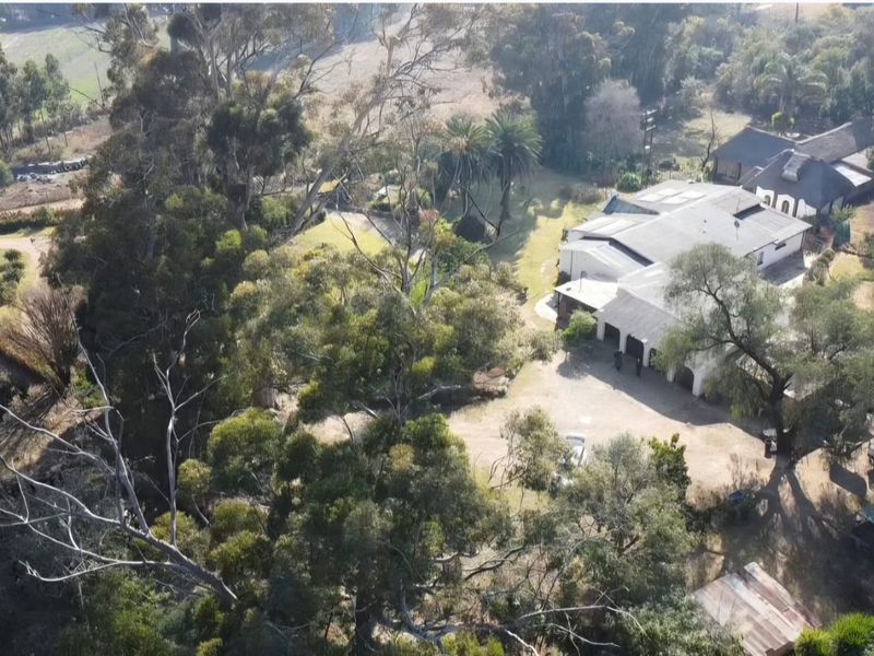 Aerial view of a farm property featuring a large residence with a thatched roof, expansive grounds, and mature trees.