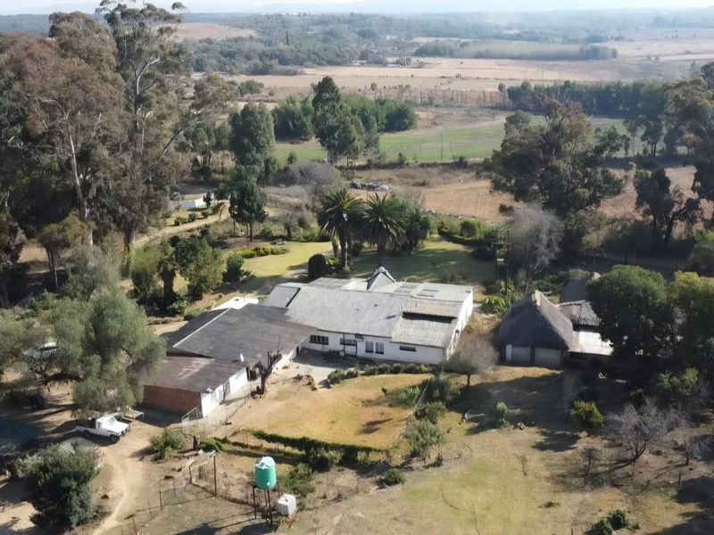 Aerial view of a rural farm property featuring a main residence, outbuildings, established trees, and surrounding agricultural land.