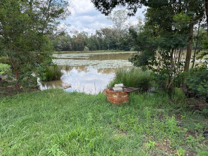 A scenic view of a natural pond on the farm property, featuring a rustic brick fire pit area nestled among the trees.