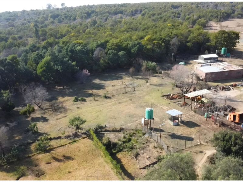 Aerial view of a farm property featuring multiple outbuildings, water storage tanks, and expansive open land surrounded by established trees.