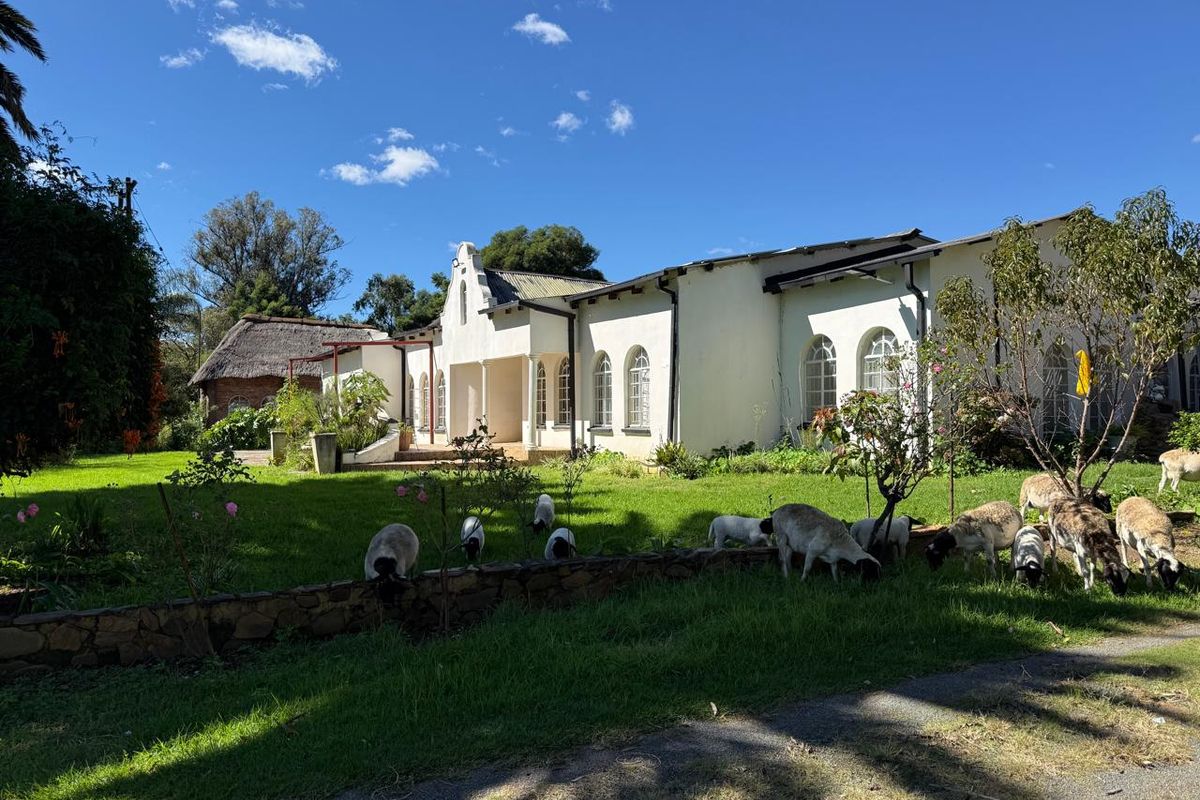 A view of the rear farmstead elevation featuring white gabled architecture, arched windows, and a landscaped garden with a stone retaining wall.