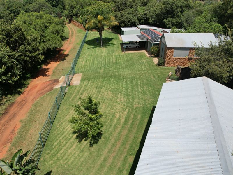 Aerial view of a farm property featuring a large lawn, stone-walled outbuilding with solar panels, and a dirt access road.