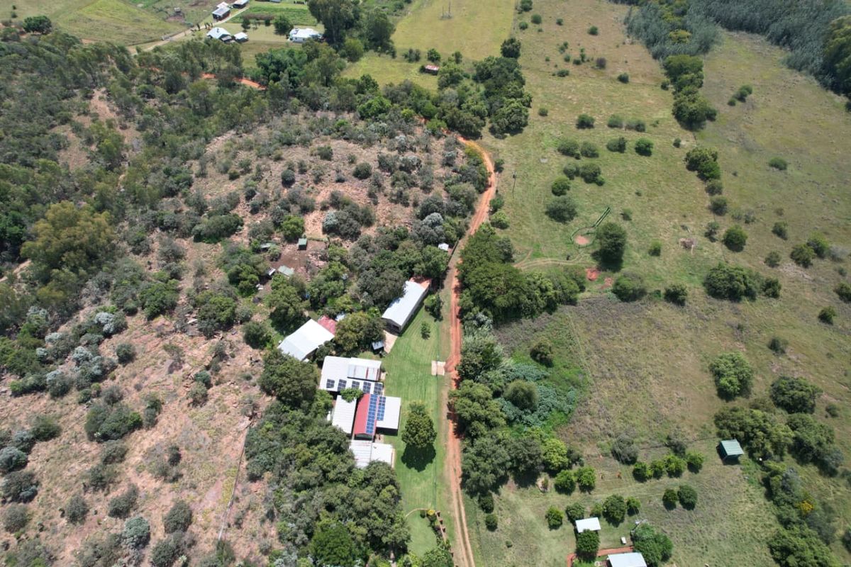 Aerial view of a rural farm property featuring multiple outbuildings, solar panel installations, and extensive surrounding pasture and woodland.