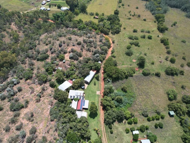 Aerial view of a rural farm property featuring multiple outbuildings, solar panel installations, and extensive surrounding pasture and woodland.